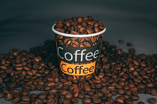 A closeup shot of a printed cup full of roasted coffee beans on dark backgroun