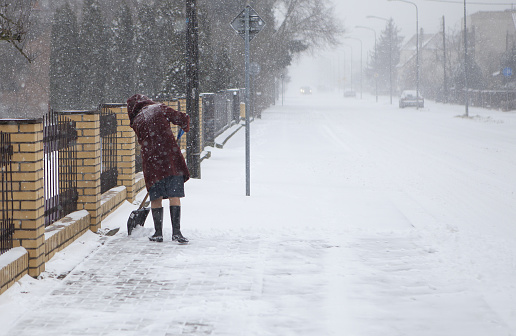 Poznań, Poland – February 08, 2021: Woman with shovel cleaning snow. Winter shoveling. Removing snow after blizzard