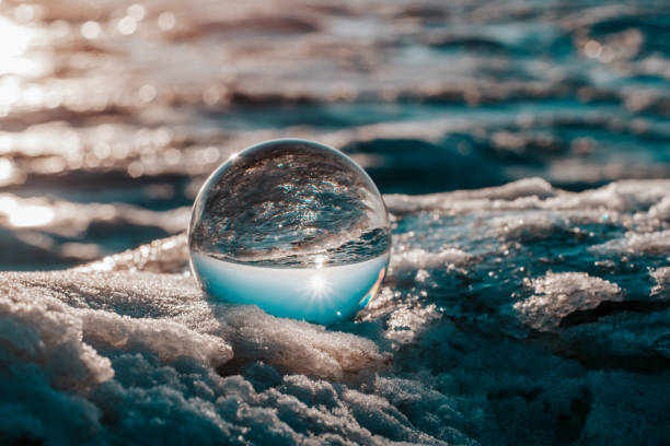 kristallkugel auf dem eis reflektiert den blauen himmel und die eisige oberfläche - ice crystal winter nature ice stock-fotos und bilder