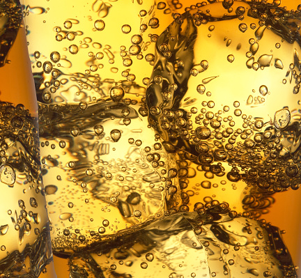 A closeup shot of ice and bubbles in a yellow liquid