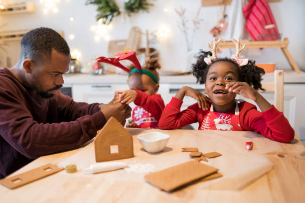 African American family decorating a gingerbread house together on Christmas day. Christmas moments with kids at home concept