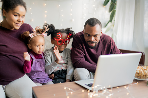 Online Family Reunion. Happy african american family with two kids making engaging and fun video call with friends or grandparents during winter holidays at home.  Online celebrating.