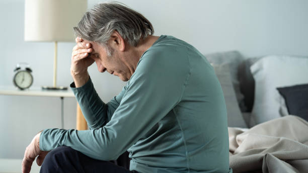 istock Old man holding his head with his hands sits on the bed 1441856900