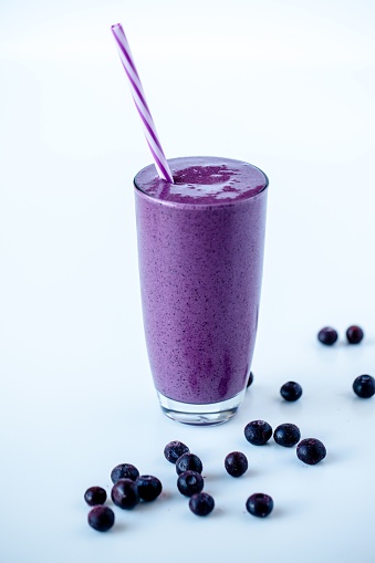 a Vertical shot of a blueberry milkshake in a  glass mug on white surface