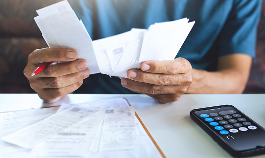 Stressed asian man using smartphone calculating receipt payment, monthly expenses, taxes, bank account balance and , Income is not enough, no money in pocket for expenses