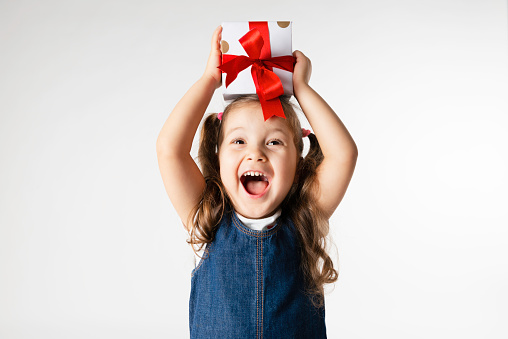 Caucasian girl is holding a gift box over her head and expresses happiness.