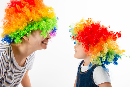 Cute little girl and young female adult are wearing a clown wig and looking at each other in front of white background.