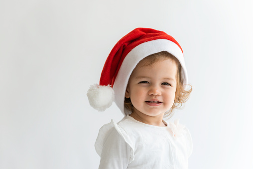 Little girl with santa hat is looking at camera in front of white background.
