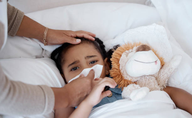 istock Sick child, concerned mother and covid symptoms while in bed for health problem or fever while wiping nose with tissue. Woman caring for sad girl with virus, cold or flu in bedroom at home 1441866717