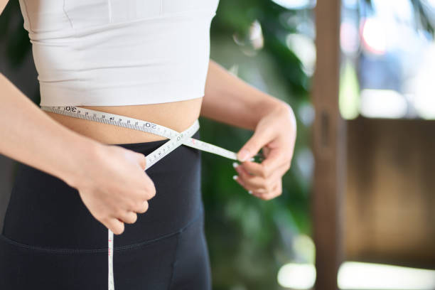 Asian woman measuring her waist size with a tape measure Asian woman measuring her waist size with a tape measure dieting stock pictures, royalty-free photos & images