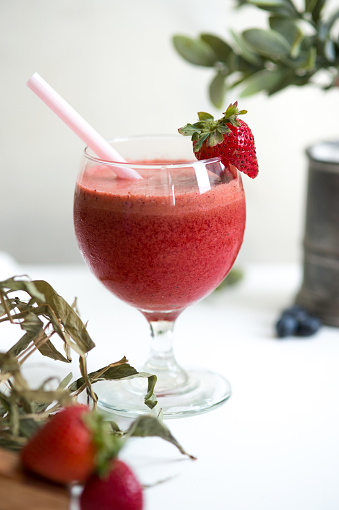 A strawberry smoothie served in a glass with strawberry garnish