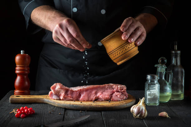 un chef professionnel prépare de la viande de veau crue. avant la cuisson, le chef ajoute du sel au bœuf. un plat national est en cours de préparation dans la cuisine du restaurant - veal calf meat baking photos et images de collection