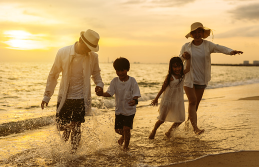 Happy asian family enjoy the sea beach at consisting father, mother,son and daughter having fun playing beach in summer vacation on the ocean beach. Happy family with vacations time lifestyle concept.