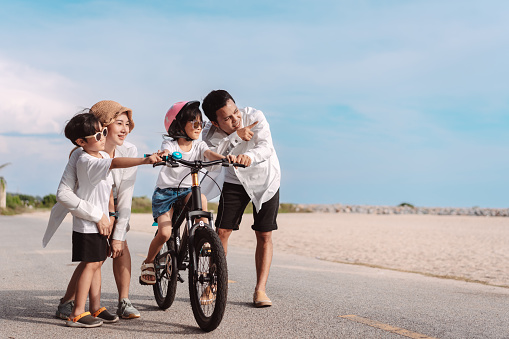 Family on the beach they are enjoy bicycle. Happy father, mother and son, daughter enjoying road trip the summer holidays.Parents and children are riding on a bicycle with a sea travel trip exercise