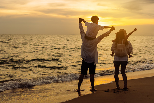 Happy asian family on the beach in holiday. of the family holding hands, Son and daughter piggyback on parents.They are having fun playing enjoying the sunset on the beach. Summer Family and lifestyle