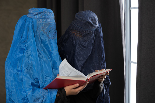 The Quran. The Holy book of Muslims. Young Asian women with burka reading the Islamic Qur'an or Koran against the dark background to close to the teachings of Prophet or God. religion and faith
