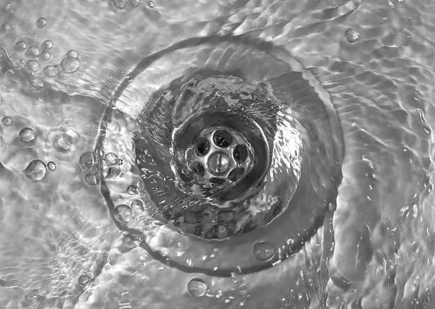 Water swirling down the plughole of a steel sink (black and white).