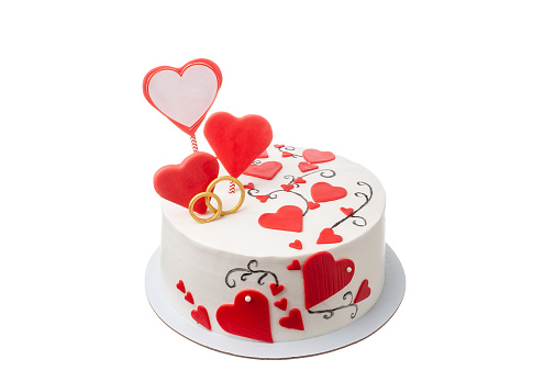 Stock photo showing elevated view of plate containing a cut, heart-shaped red velvet cake covered in butter cream and decorated with dehydrated raspberry powder and sugar sprinkle hearts, displayed against a yellow background.