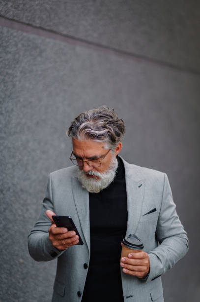 istock Senior businessman standing outside and using smartphone and drinking coffee 1441881176
