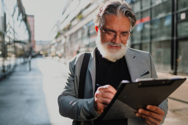 istock Senior business man standing outside and taking notes on a clipboard 1441881196