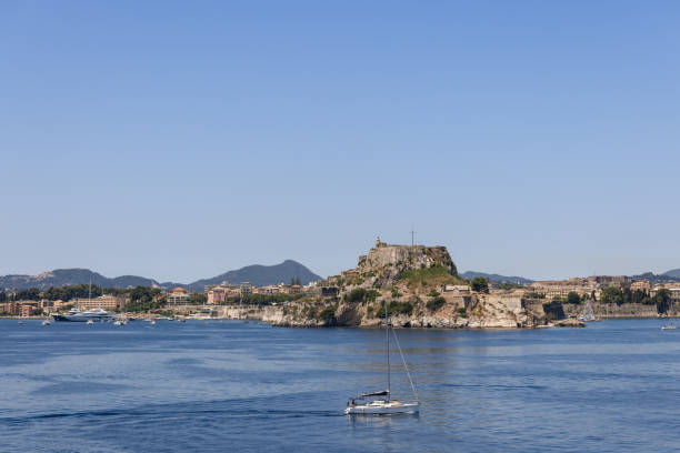 piccolo yacht bianco solitario con vele piegate sullo sfondo dell'enorme vecchia fortezza che domina tutta la regione, isola di corfù, grecia, mattina soleggiata - backdrop old fashioned outdoors yacht foto e immagini stock