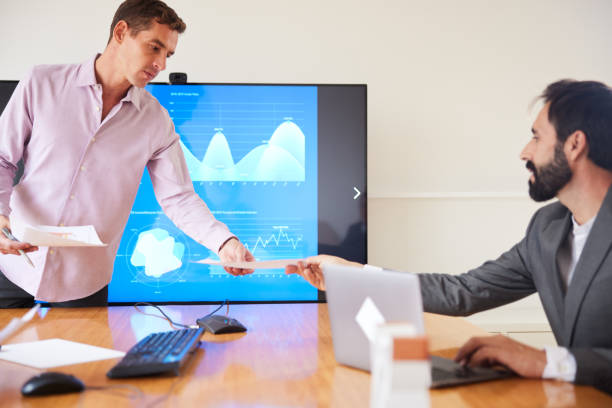 istock Handsome mid adult business presenter distributes informative handouts during presentation to mature male manager 1441882030