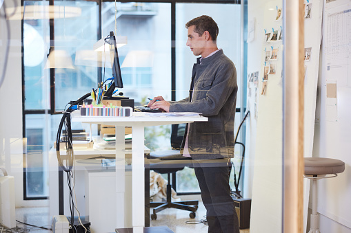 El atractivo empresario adulto medio de pelo corto está parado en una estación de trabajo flexible utilizando una PC de escritorio. photo