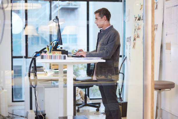 istock Attractive short-haired mid adult entrepreneur is standing at a flexible workstation using a desktop PC. 1441882065