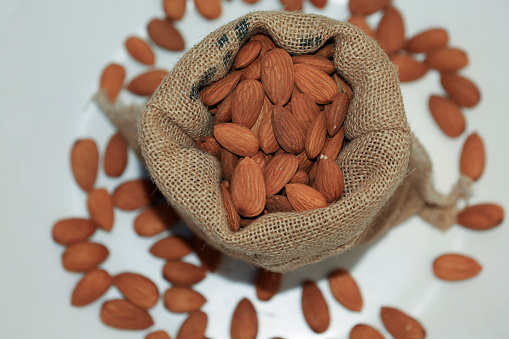 Burlap sack filled with Almonds table top view with selective focus.
