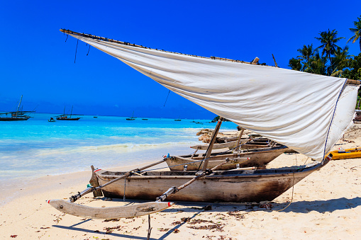 Sail boat in the sea beside the beach with clear blue sky and white sand