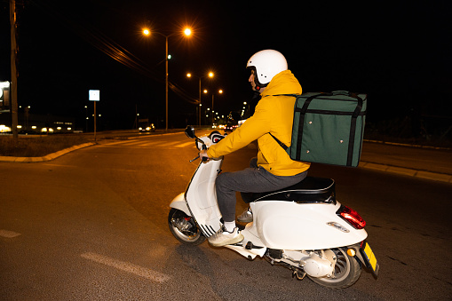 Unrecognizable Caucasian man, an delivery person, driving scooter, while delivering the orders around the city