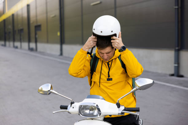 Mid-adult Caucasian man, an delivery person, on scooter, adjusting crash helmet