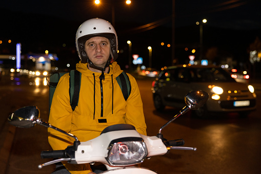 Portrait of tired Caucasian man, an delivery person, driving scooter, while delivering the orders around the city