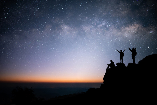Silhouette of group of young traveler standing, open arms and watched the star, milky way and night sky on top of the mountain. They enjoyed traveling and was successful when he reached the summit.