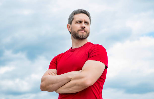istock confident man in red shirt crossed hands on sky background 1441886652