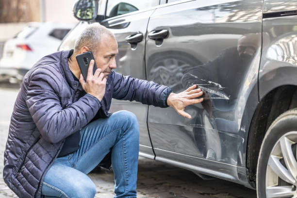 un hombre llama a la compañía de seguros o a la policía porque alguien retrocedió hacia la puerta lateral de su automóvil en el estacionamiento. - damaged car fotografías e imágenes de stock