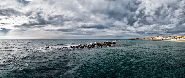 Panoramic view of bad weather and dramatic sky over Roman coast at Ostia Lido with city skyline and rough sea meanwhile a crow rests over Neptune statue.