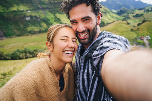 Young Colombian woman and Turkish man embracing during mountain camping and taking selfie on mountain  top