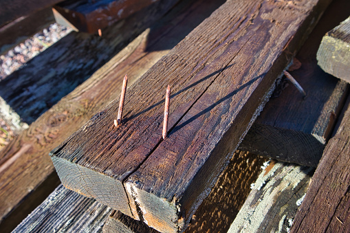 two old rusty nails sticking out of two by four wooden plank