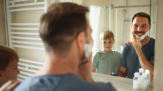Son watching his father shaving in bathroom mirror