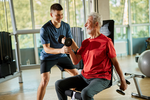 Senior man exercising with personal trainer using dumbbells the gym