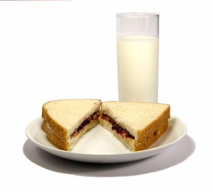 peanut butter and jelly sandwich on plate with glass of milk isolated on white