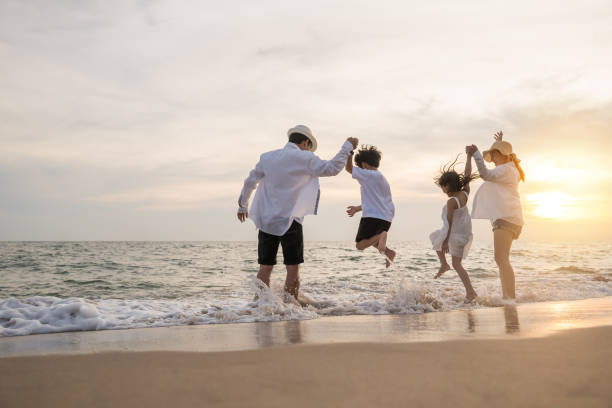 행복한 가족은 해질녘에 휴일에 해변에서 점프하는 재미를 느낍니다. 스톡 사진