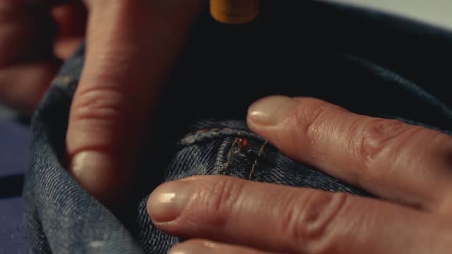 A tailor inserts metal rivets on jeans with a special machine