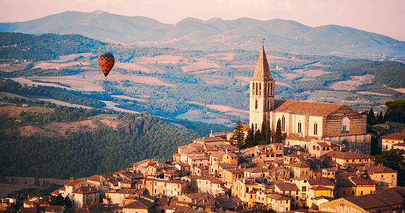 Single hot air balloon flying over a small town with a bell tower.