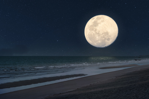 Big moon glowing over tropical sea and tranquil beach in summer at night