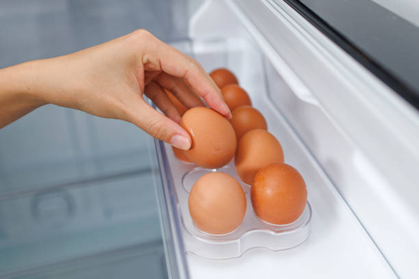 Cropped Shot Of A Woman Taking Out A Fresh Egg From The Shelf In The Refrigerator stock photo