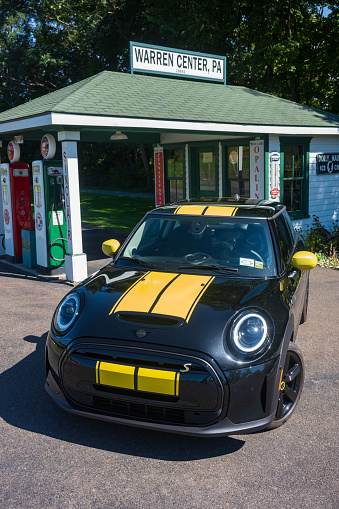 Warren Center, PA, USA - Sept 24, 2022: A black and yellow 2023 MINI Cooper SE, an electric vehicle, is photographed near a vintage gas station located in a rural town. Are EVs a fad or here to stay?