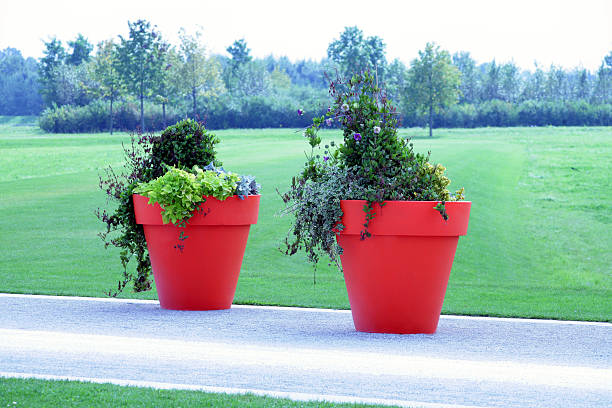 Two huge red flowerpots on a street. 