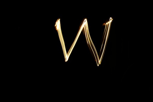 Letter W. Light painting alphabet. Long exposure photography. Drawing letter W with gold lights against black background.